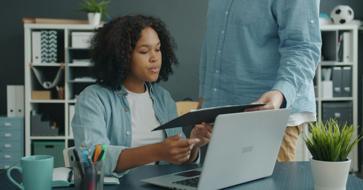 Two colleagues reviewing business documents at a desk with a laptop