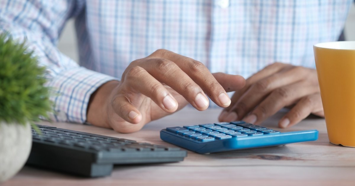 Person using a calculator at a desk with papers and a coffee mug